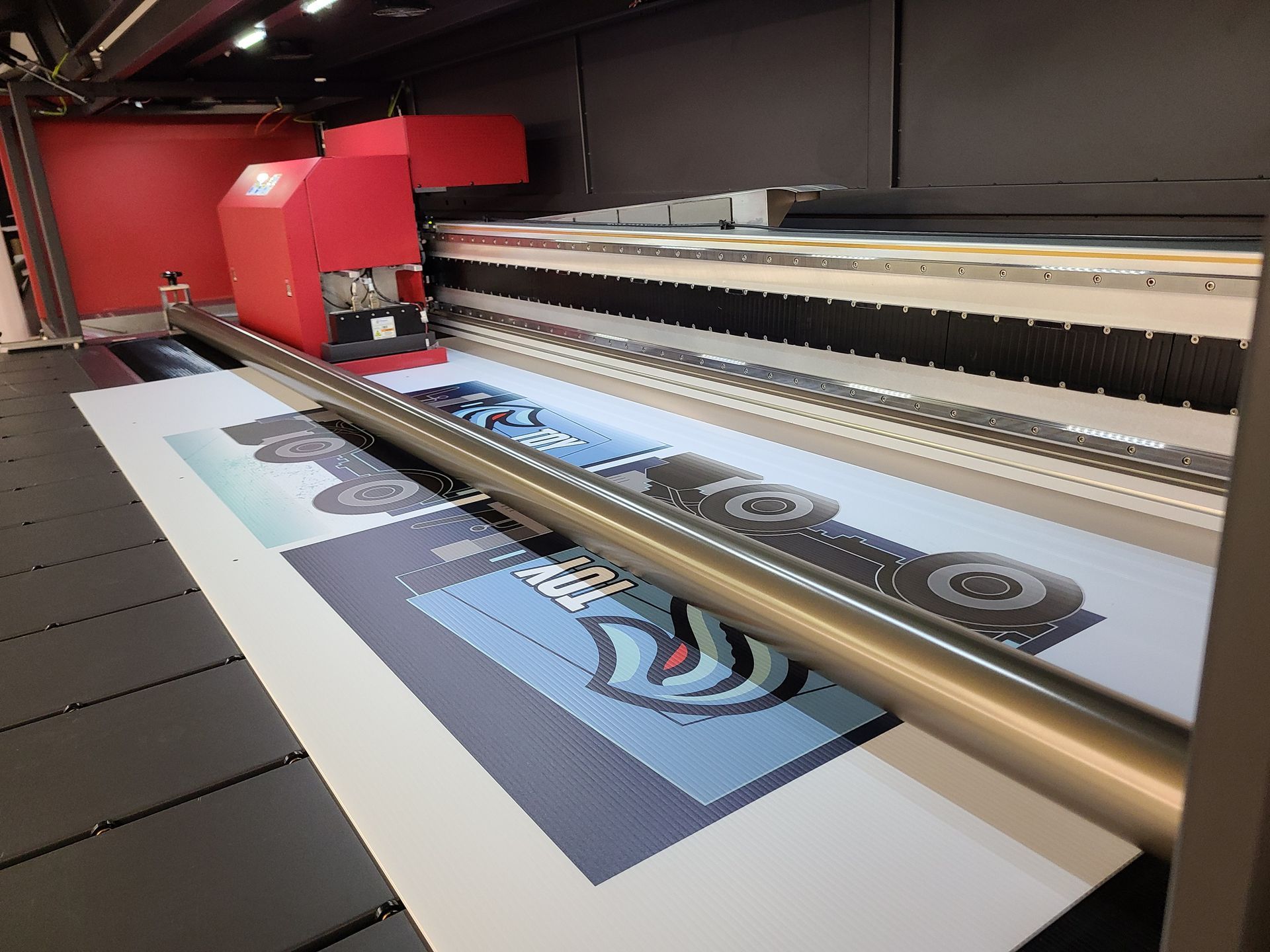 Large-format printer printing a colorful poster on white paper in a workshop