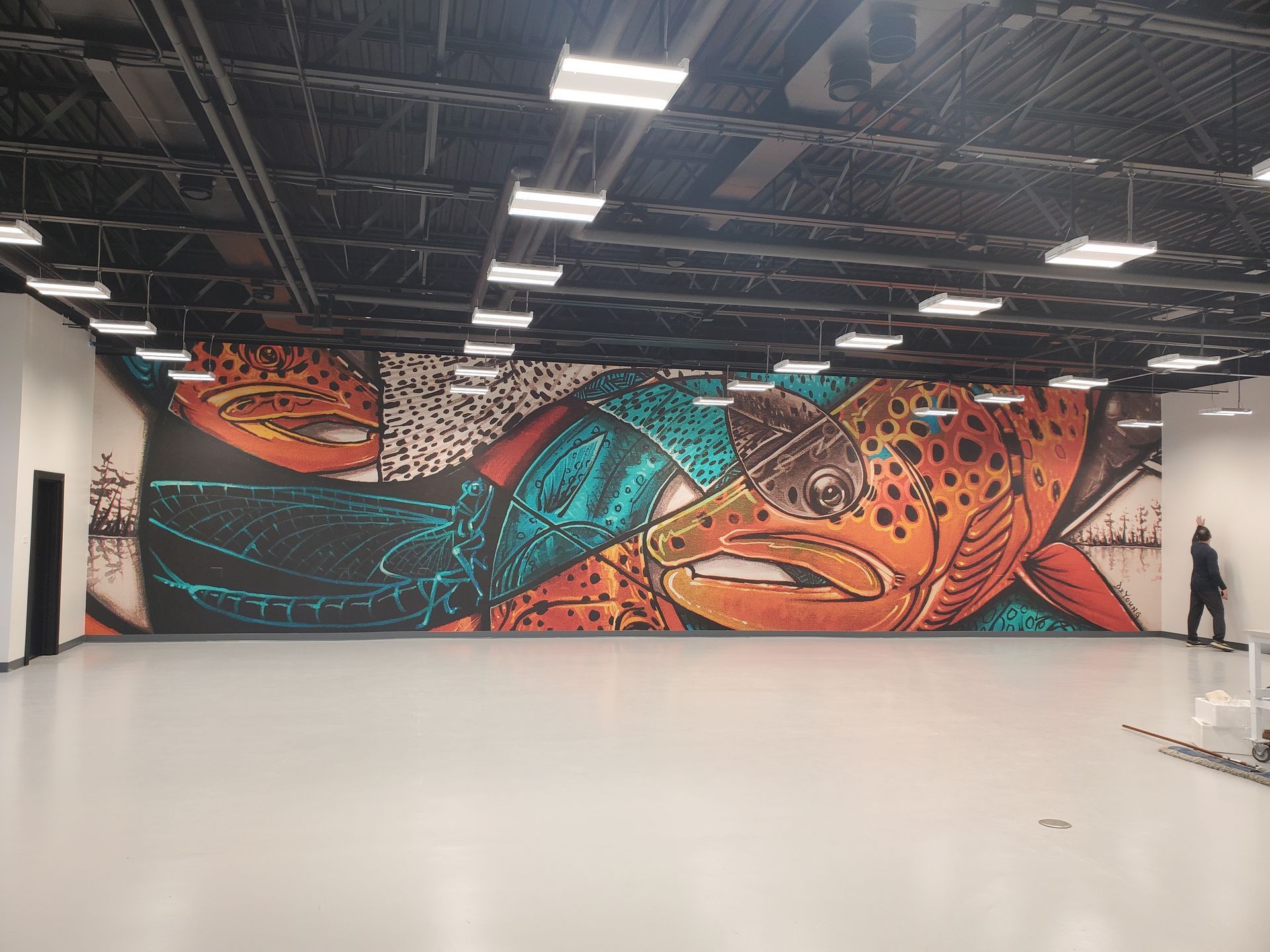 Large mural of a fish on a wall in a large, empty room with a person standing by the right side.