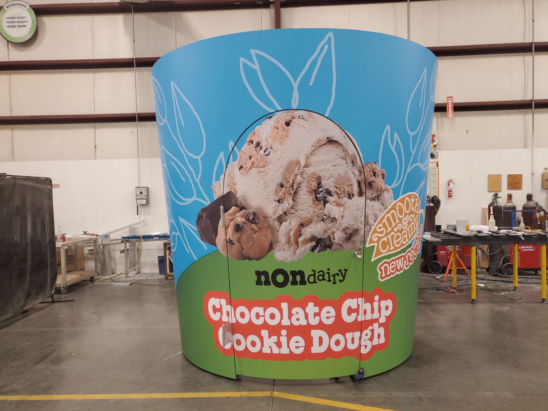 Giant cylindrical Ben & Jerry's Non-Dairy Chocolate Chip Cookie Dough ice cream tub display in a warehouse.