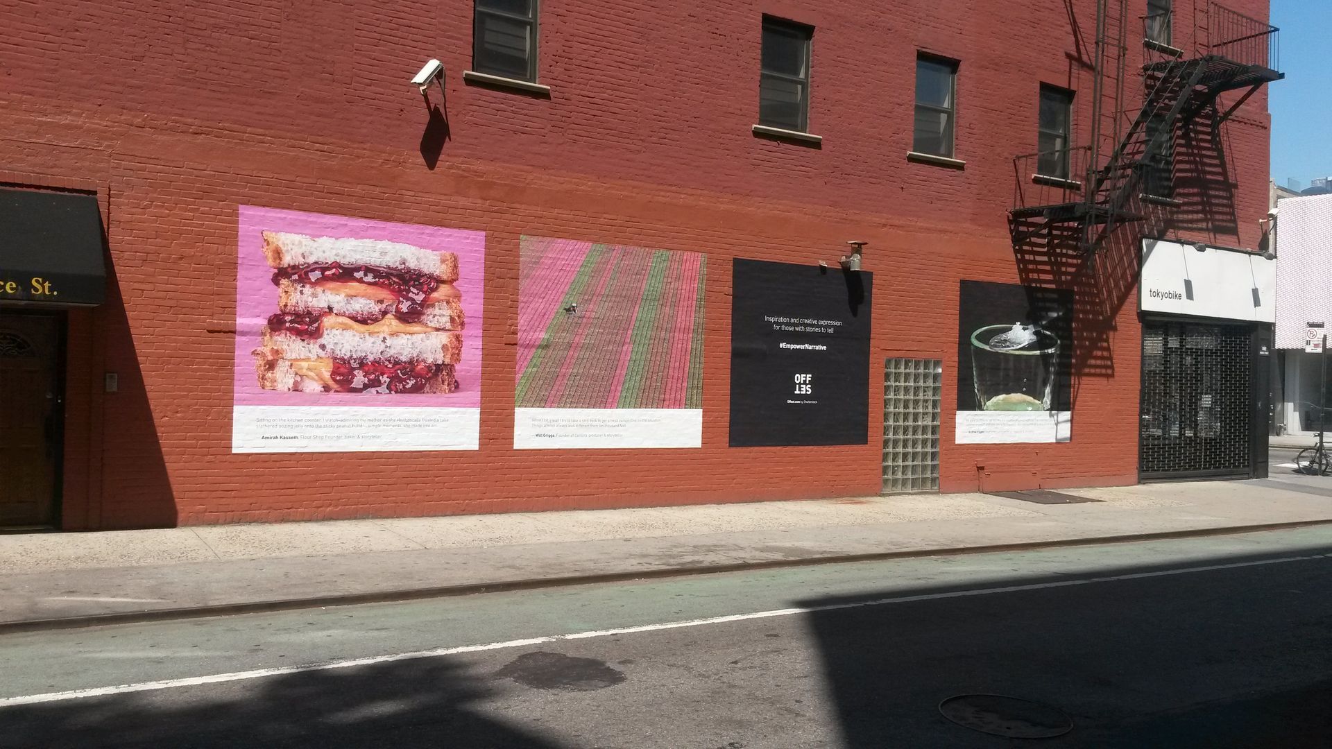 Red brick building with colorful posters and a black door on a sunny street.