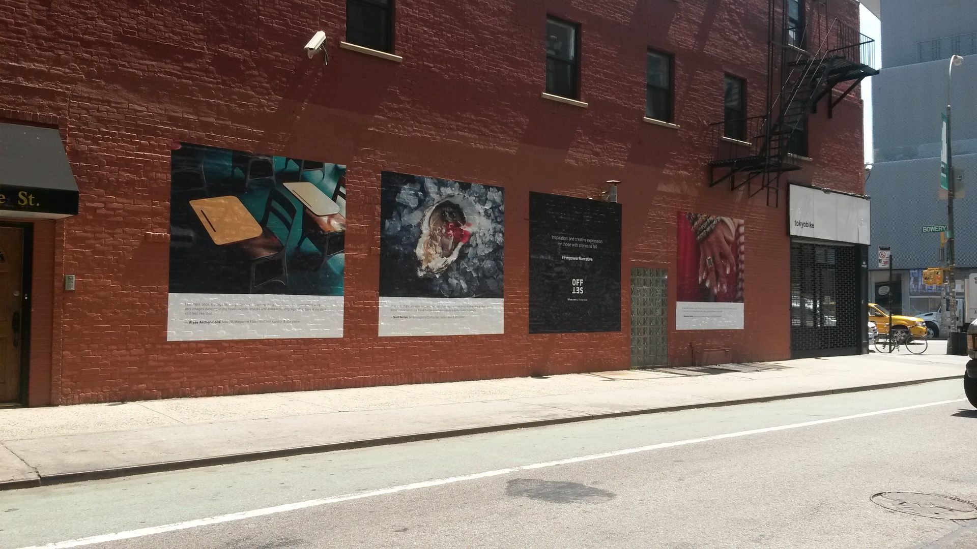 Building facade with four large posters on brick wall; street and sidewalk in foreground.