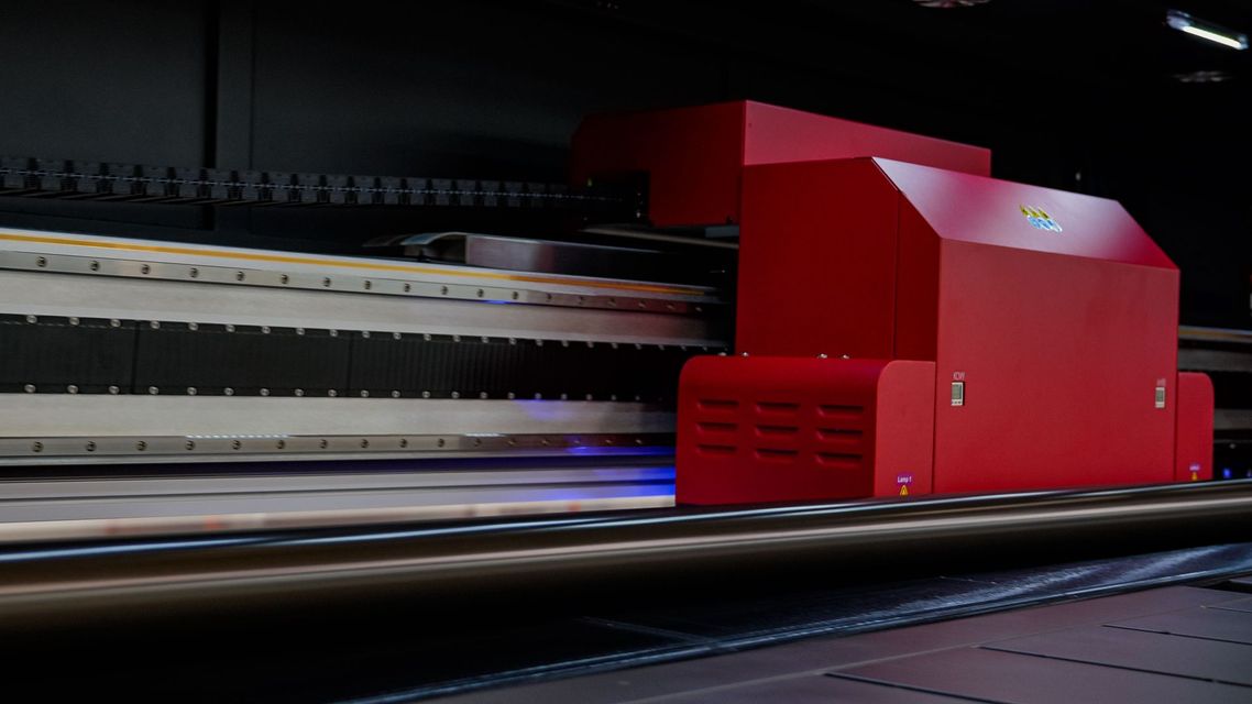 Large red industrial printer in a dark room, printing on a flat surface.