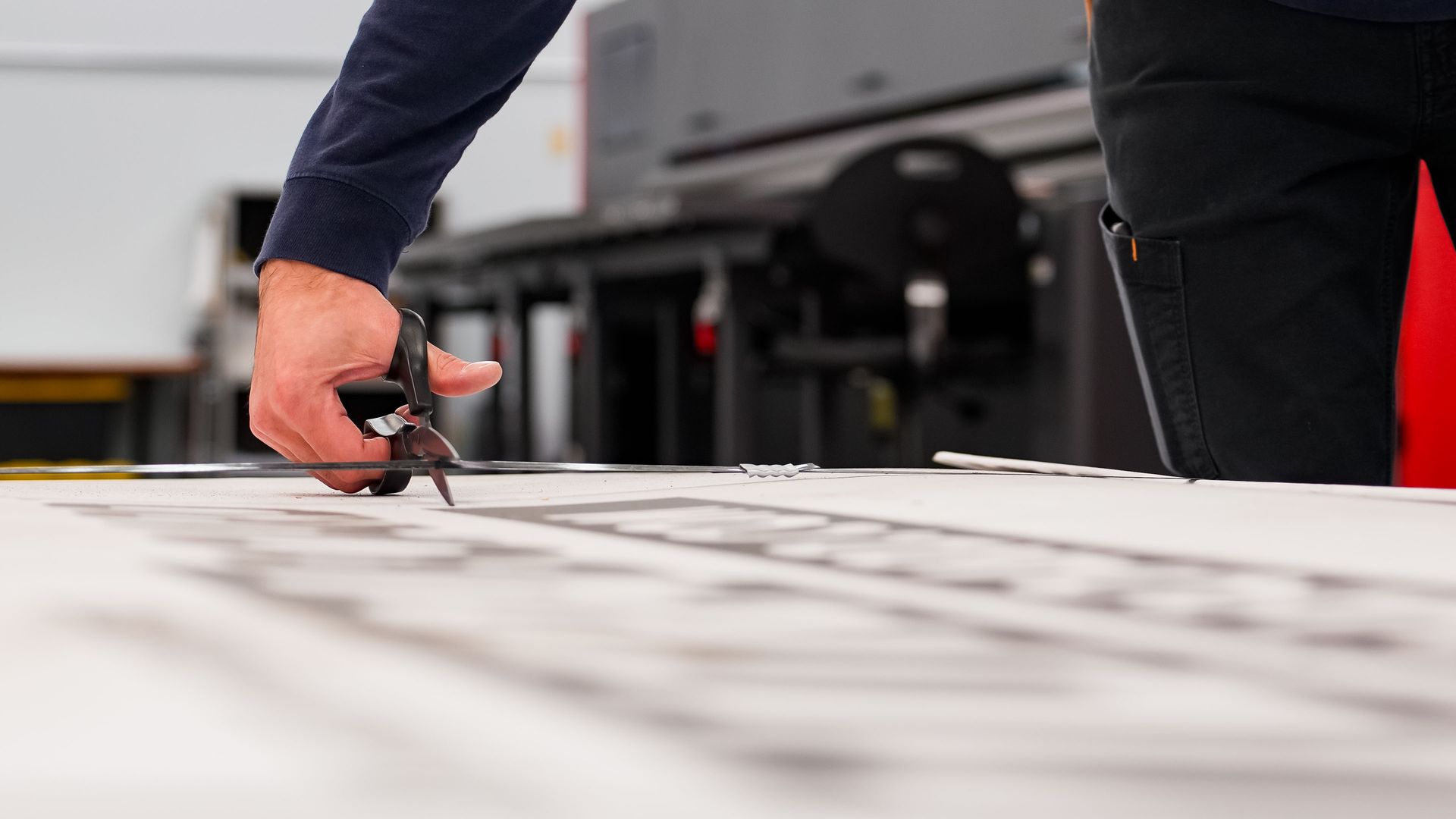 Person using scissors to cut a printed design on a large white surface.