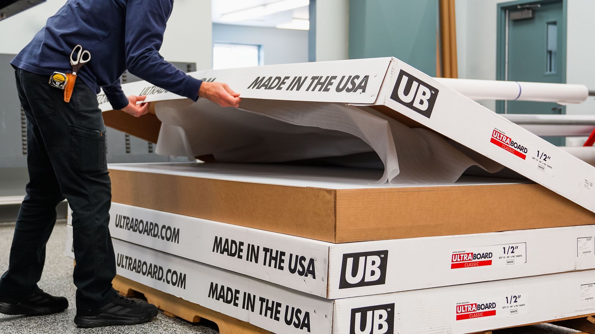 Person using a lift to load large white “Made in the USA” wrapped panels onto a truck.