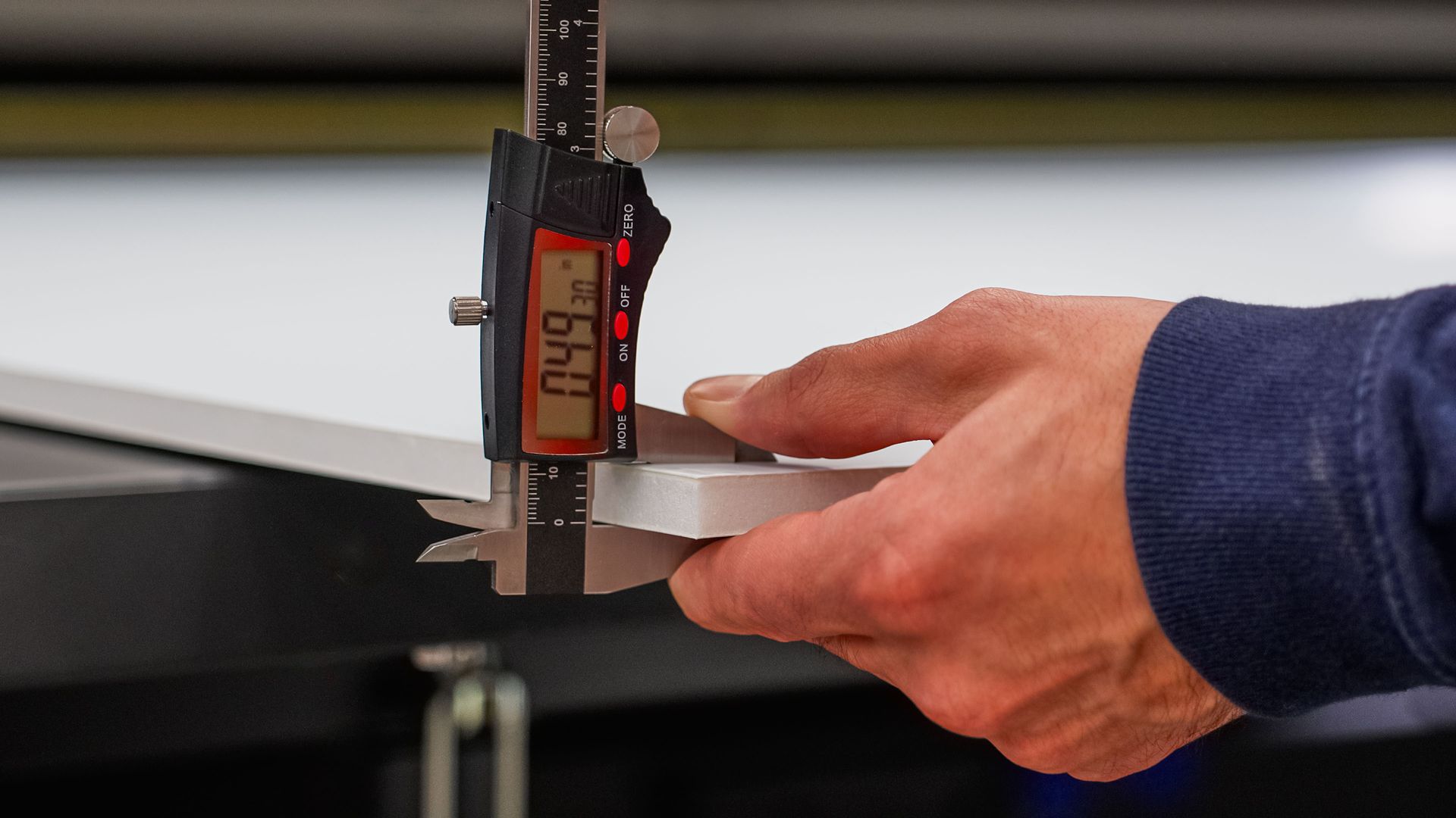 Hand using digital calipers to measure the thickness of a white piece of material, display reads 0.49.