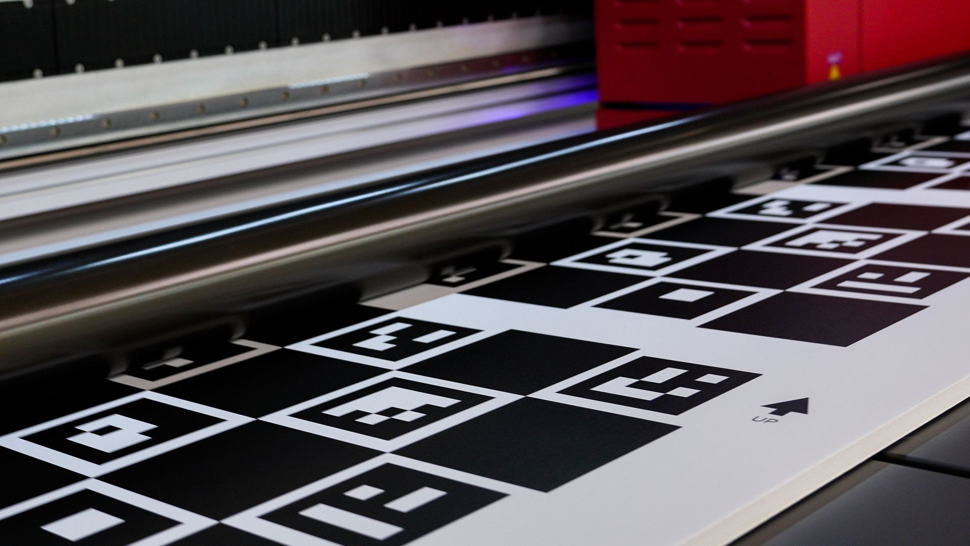 Close-up of a printing machine with a pattern of black and white square markers on the paper being printed.