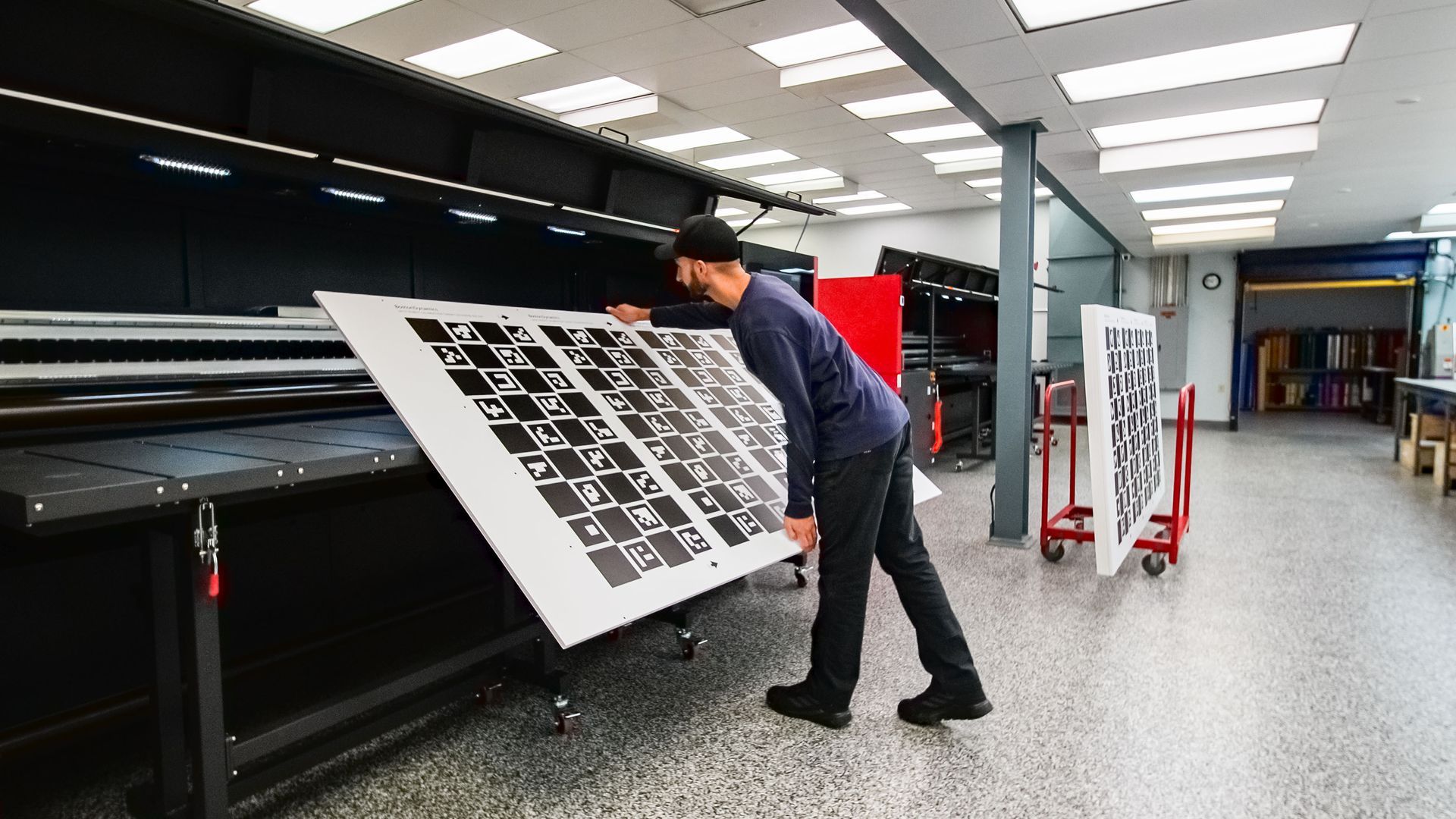 A person inspecting a large printed pattern sheet in a workshop.  Black and white patterns, indoor setting.