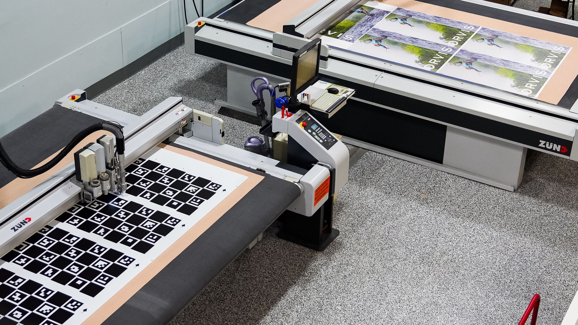 Two large industrial cutting machines on a speckled floor, cutting large printed sheets with patterns.