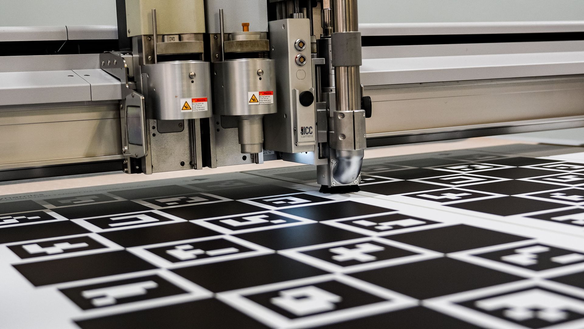 Automated cutting machine processing a large sheet with black and white markers.