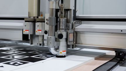 A CNC machine cutting a patterned sheet; close-up of the tool head over the material.