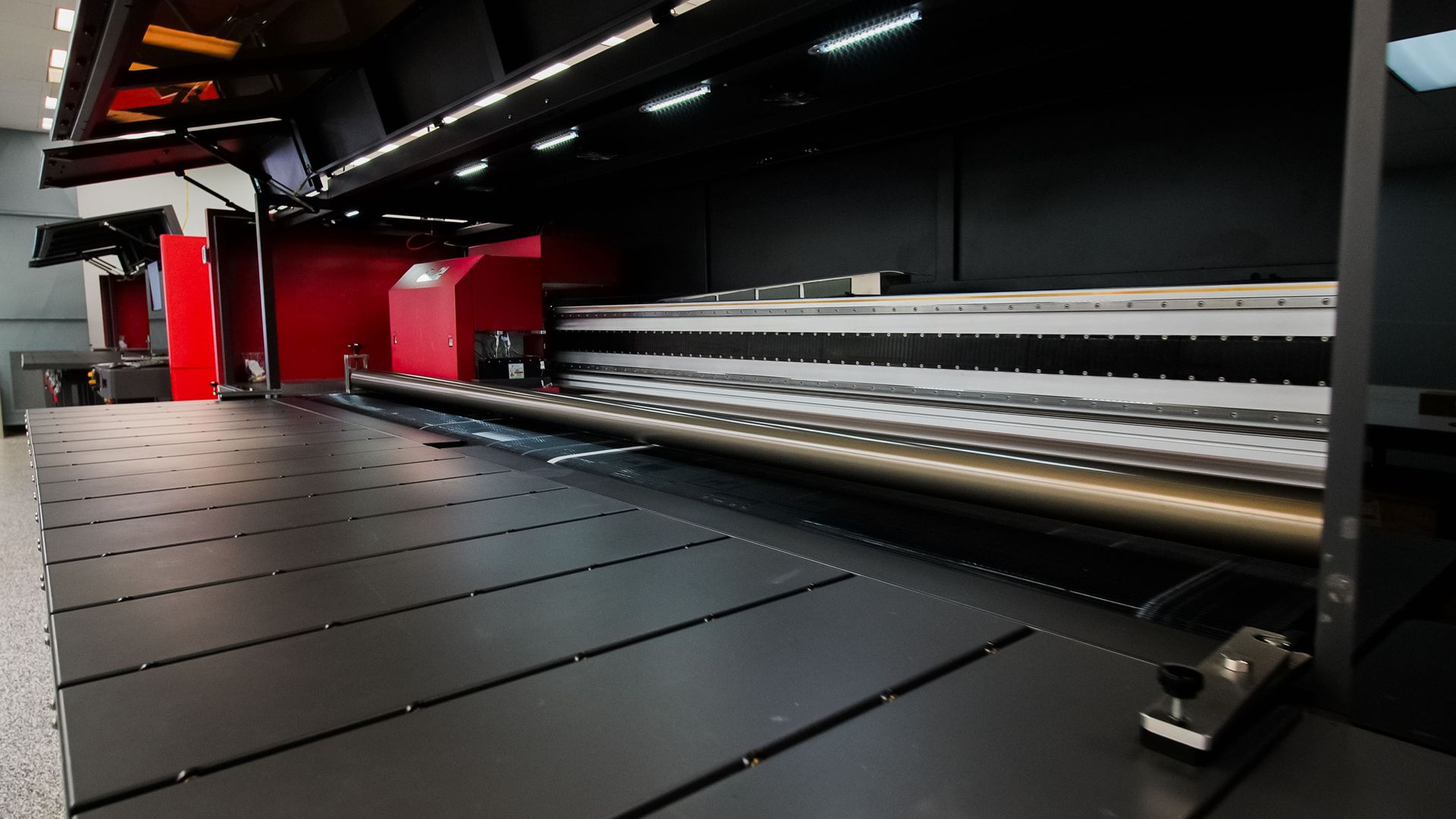 Large industrial printer with black material sheets in a red and black print shop