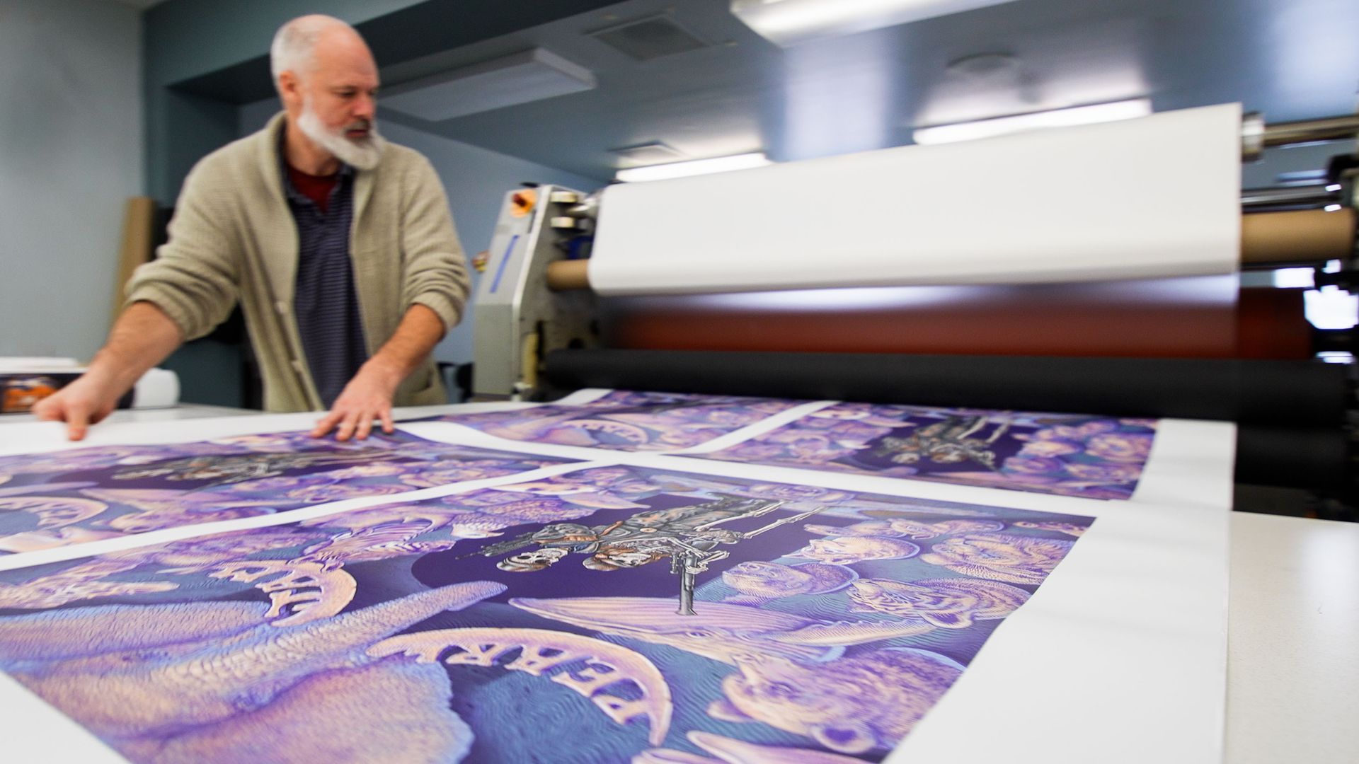 Man printing large purple and white artwork on a wide-format printer in a workshop.