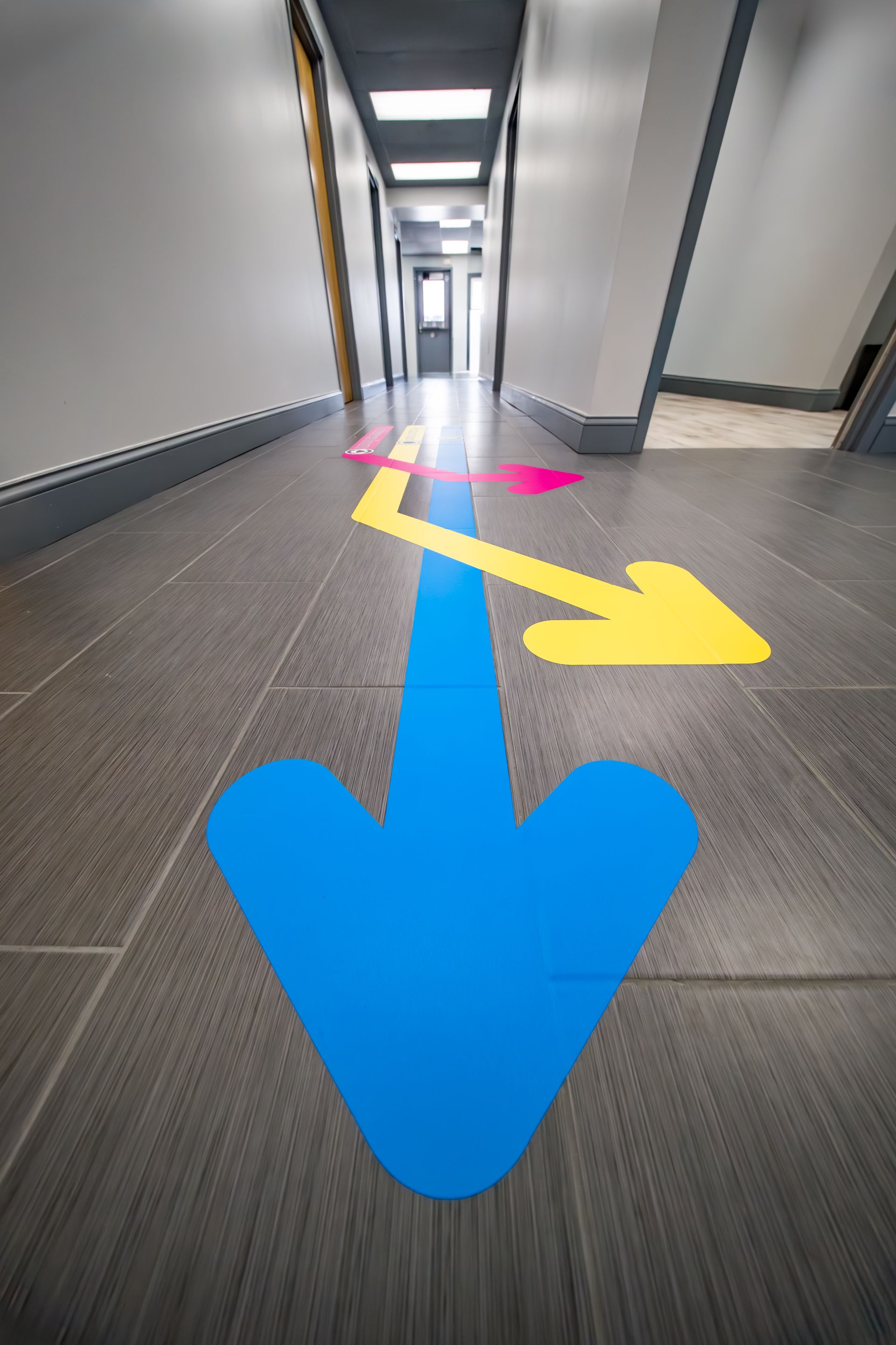 Hallway with large blue, yellow, and pink directional arrows on the floor pointing forward and right