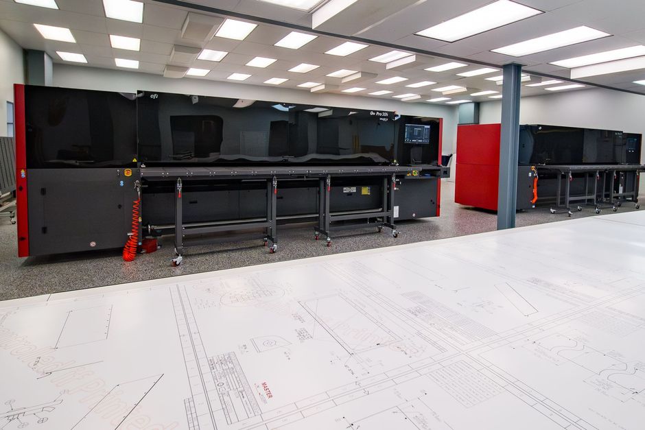 Two large, red and black industrial machines in a white-floored room with bright lights and a support column.