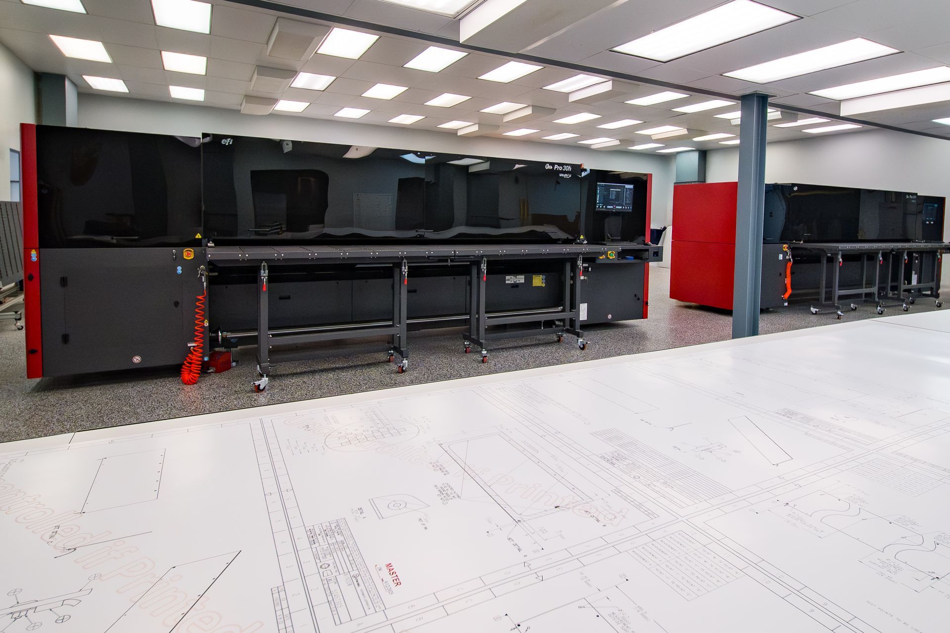 Empty server room with black cabinets, red supports, and a white tiled floor under bright ceiling lights