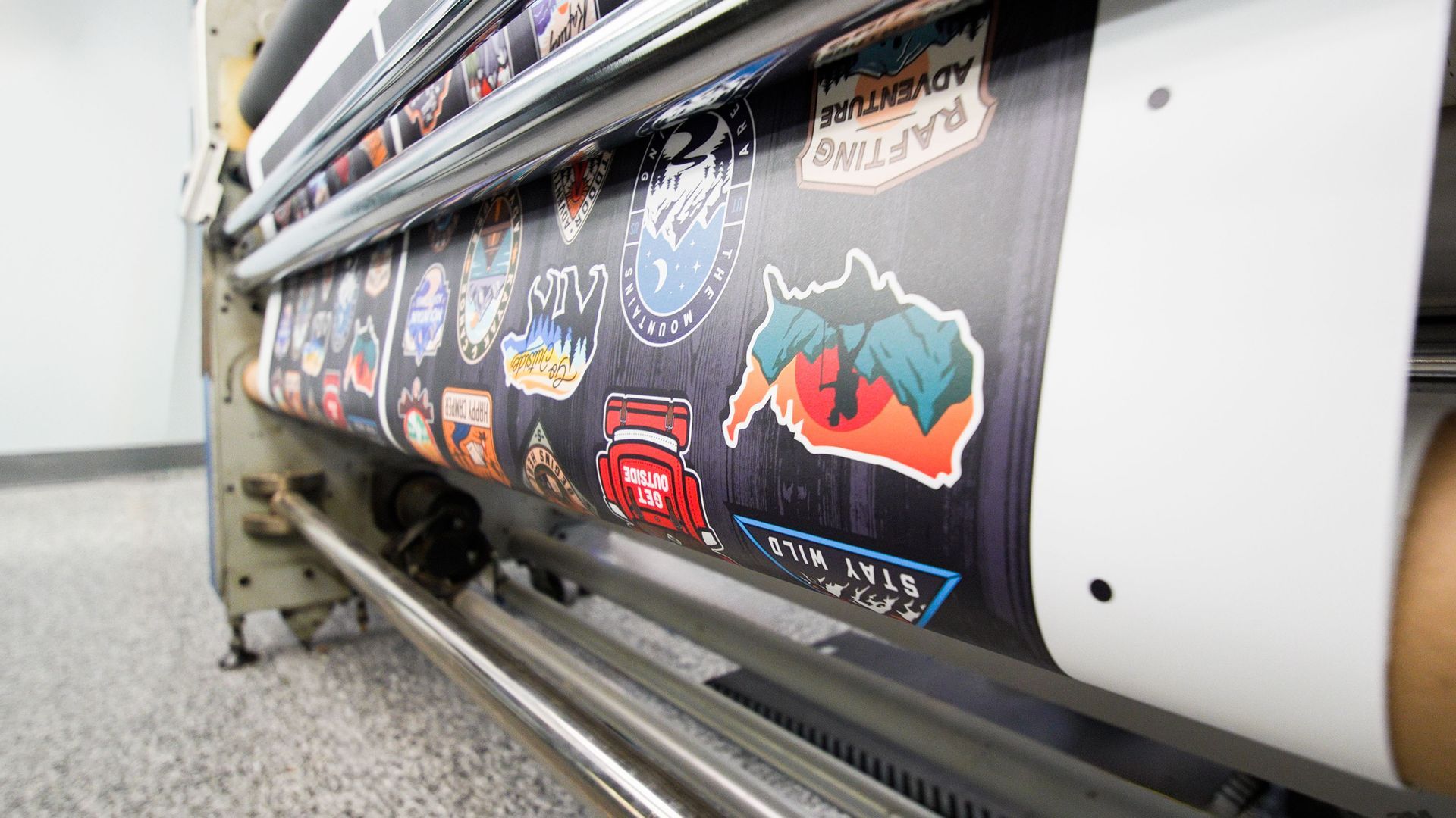 Large-format printer outputting a sticker-covered banner in a workshop