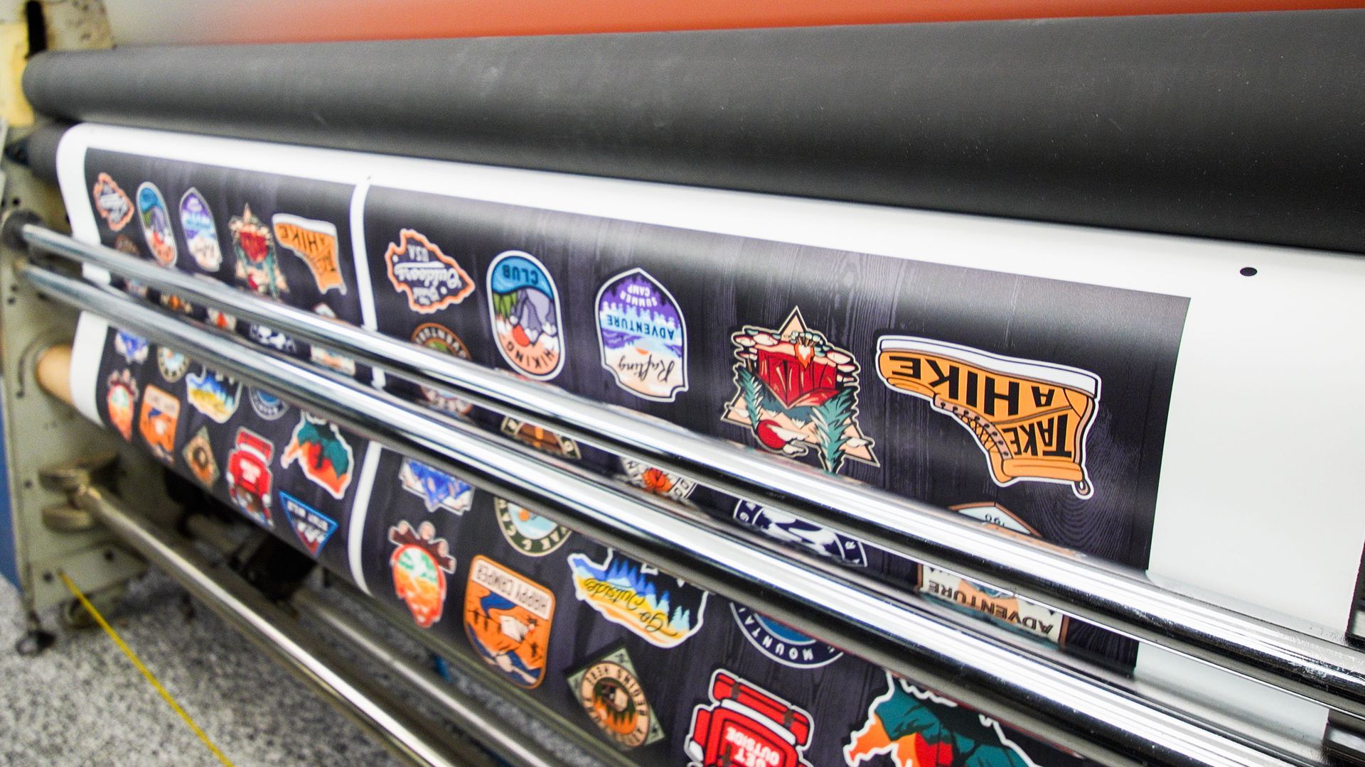 Vinyl banner with rows of colorful logos and stickers on a printing machine