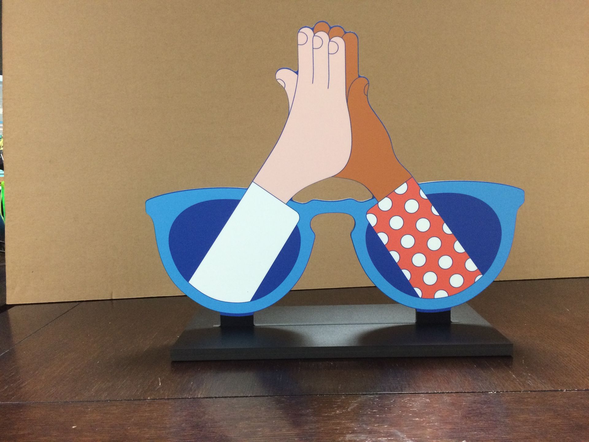 Stylized artwork of two hands pressed together, one blue sleeve and one red polka-dot sleeve, on a stand