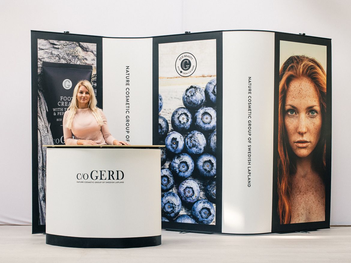 Promotional display stand with beauty ads, blue berries, and model portraits in black, white, and tan panels