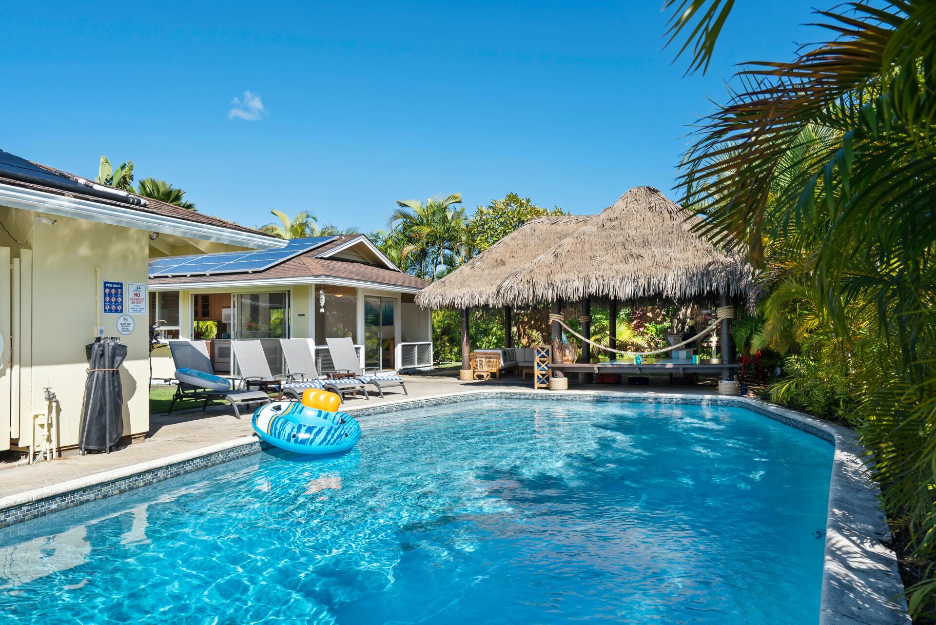 Una gran piscina frente a una casa con techo de paja.