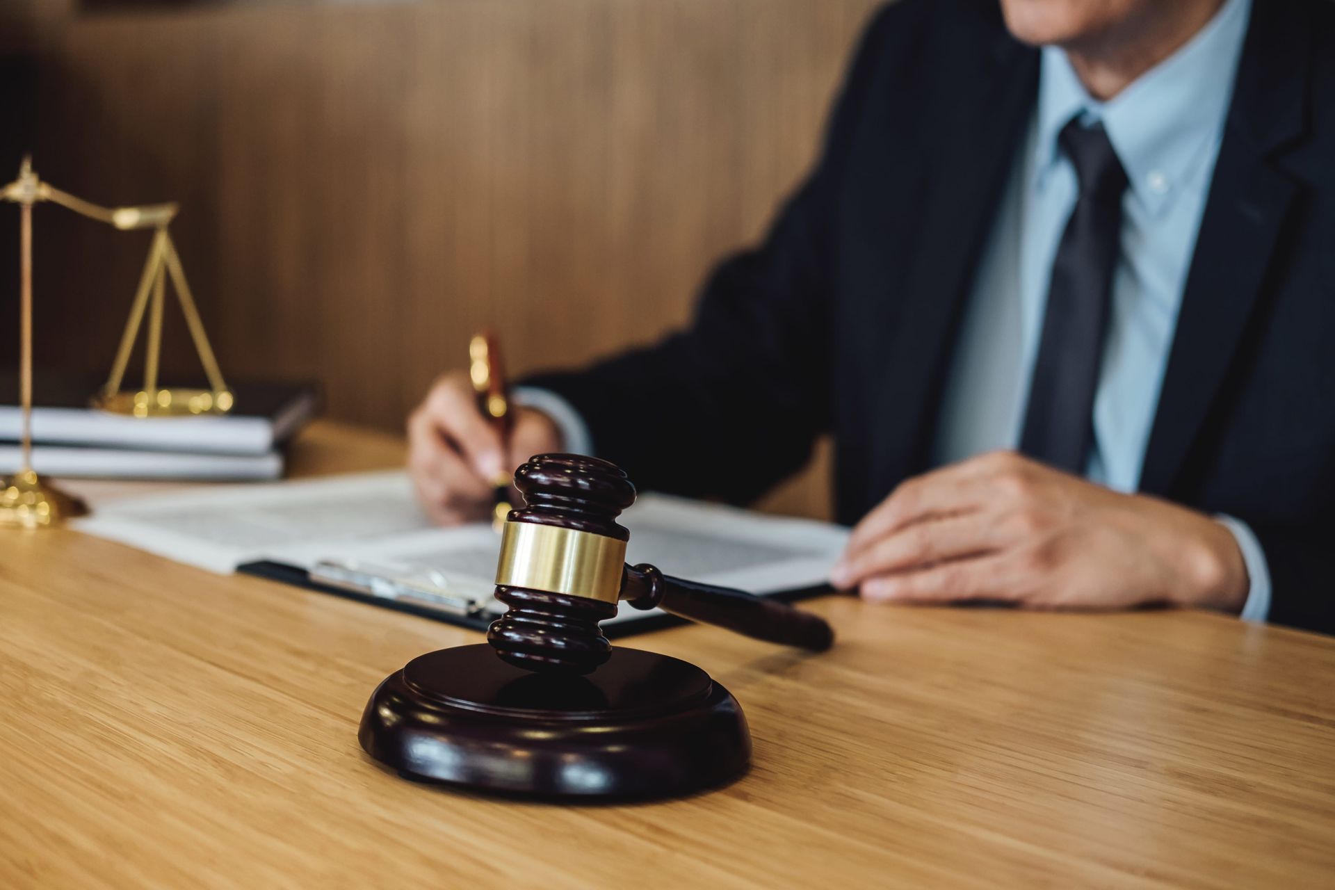 Gavel on a desk in a law office, with a suited person writing and scales of justice nearby