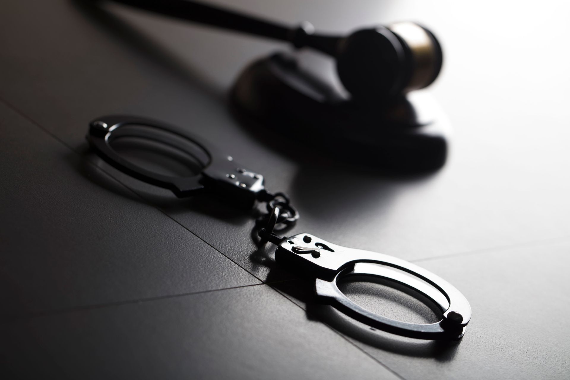 Handcuffs on a dark table with a judge’s gavel in the background, lit dramatically