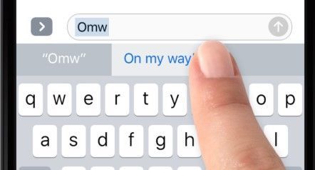 Hand selecting "On my way" from predictive text on a mobile keyboard; the phrase is highlighted in blue.