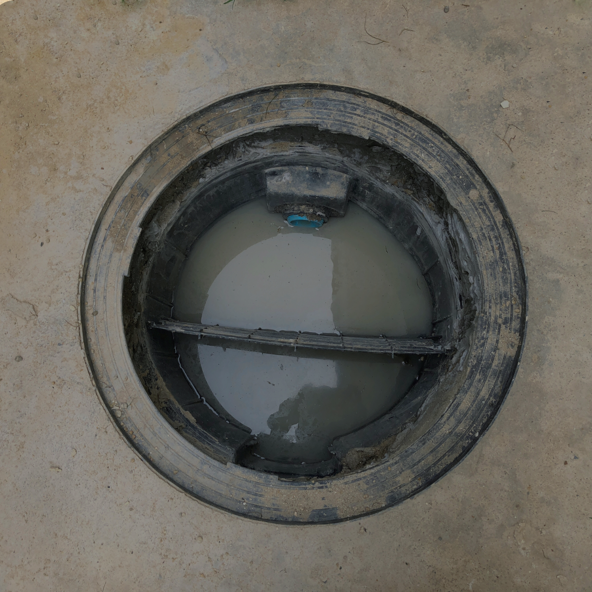 Ralo circular aberto, cheio de água turva, fixado em concreto.