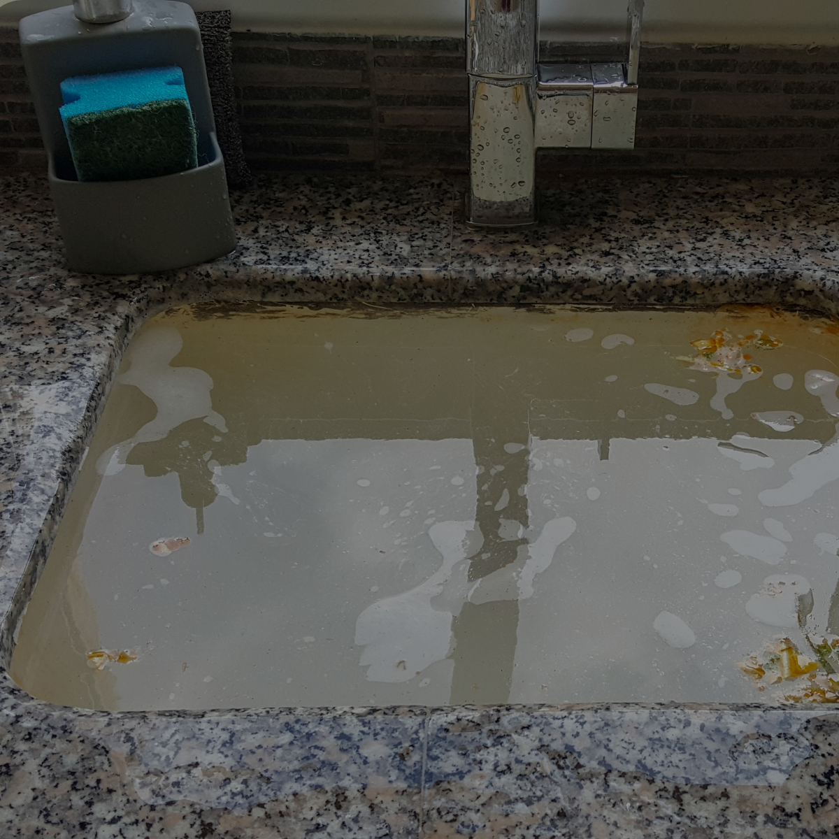 A pia da cozinha está cheia de água marrom turva, com esponja e torneira presentes.