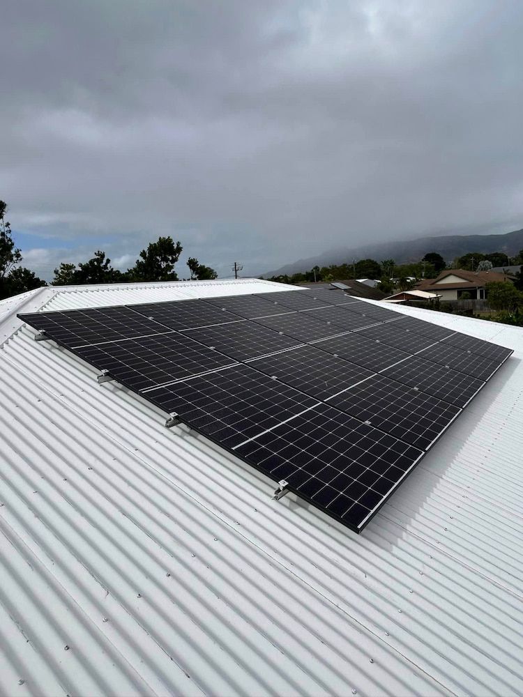 Solar panel array on a corrugated metal roof in Townsville, with hills and houses visible in the distance