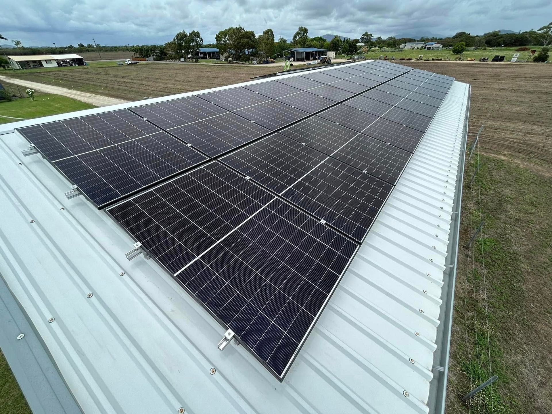 Solar Panels Mounted on a White Metal Roof in a Rural Field Under Cloudy Skies — Central Solar Services in Garbutt, QLD
