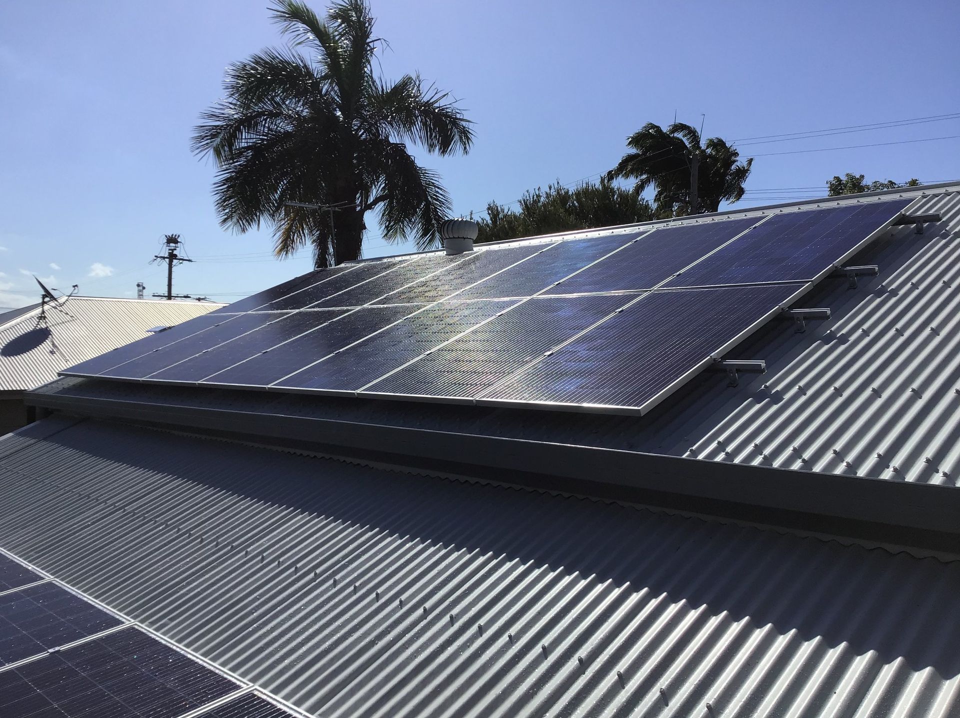 Solar panels installed on a corrugated metal roof in Queensland, capturing sunlight under a blue sky