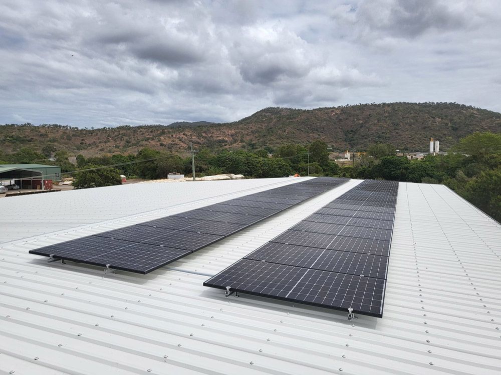Solar Panels Mounted on a White Rooftop With Hills and Cloudy Sky in the Background — Central Solar Services in Garbutt, QLD