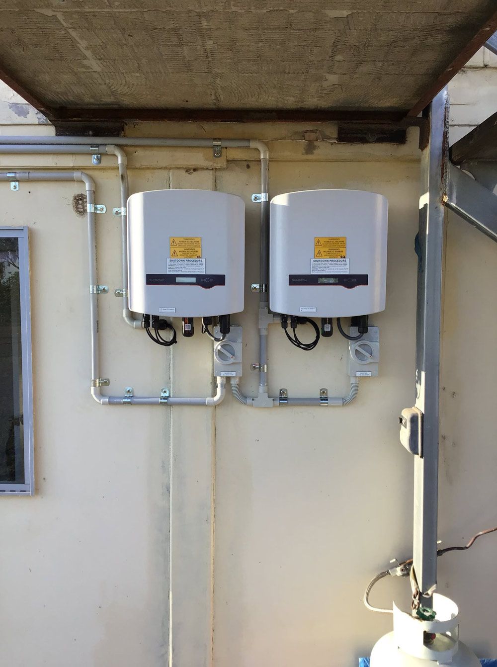 Two solar inverters mounted side by side under an eave, part of a solar power system in Townsville