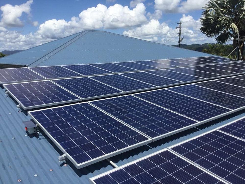 Solar panels installed on a light blue metal roof at a Townsville property under a bright blue sky