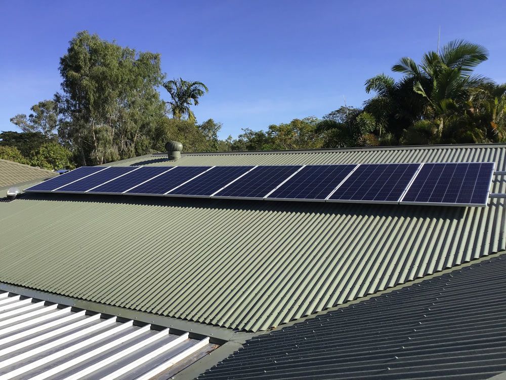 Solar Panels Mounted on a Corrugated Metal Roof Under a Clear Blue Sky — Central Solar Services in Garbutt, QLD