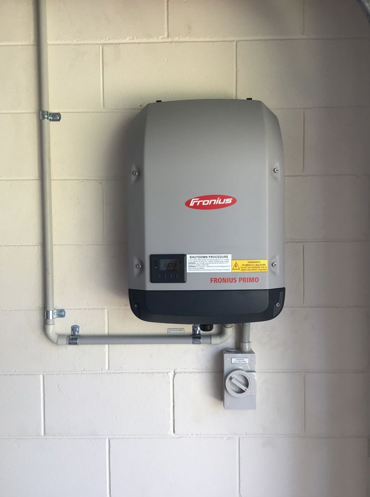 Wall-mounted Gray Electric Water Heater on a Beige Block Wall With a Switch Below — Central Solar Services in Garbutt, QLD