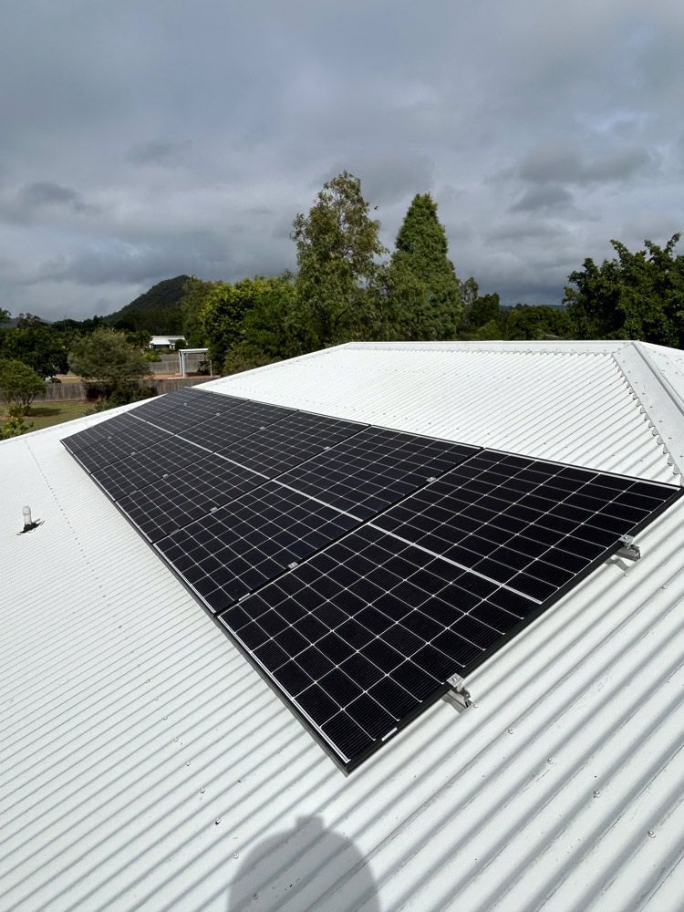 Solar Panels on a White Roof Under a Cloudy Sky, With Trees in the Background — Central Solar Services in Garbutt, QLD