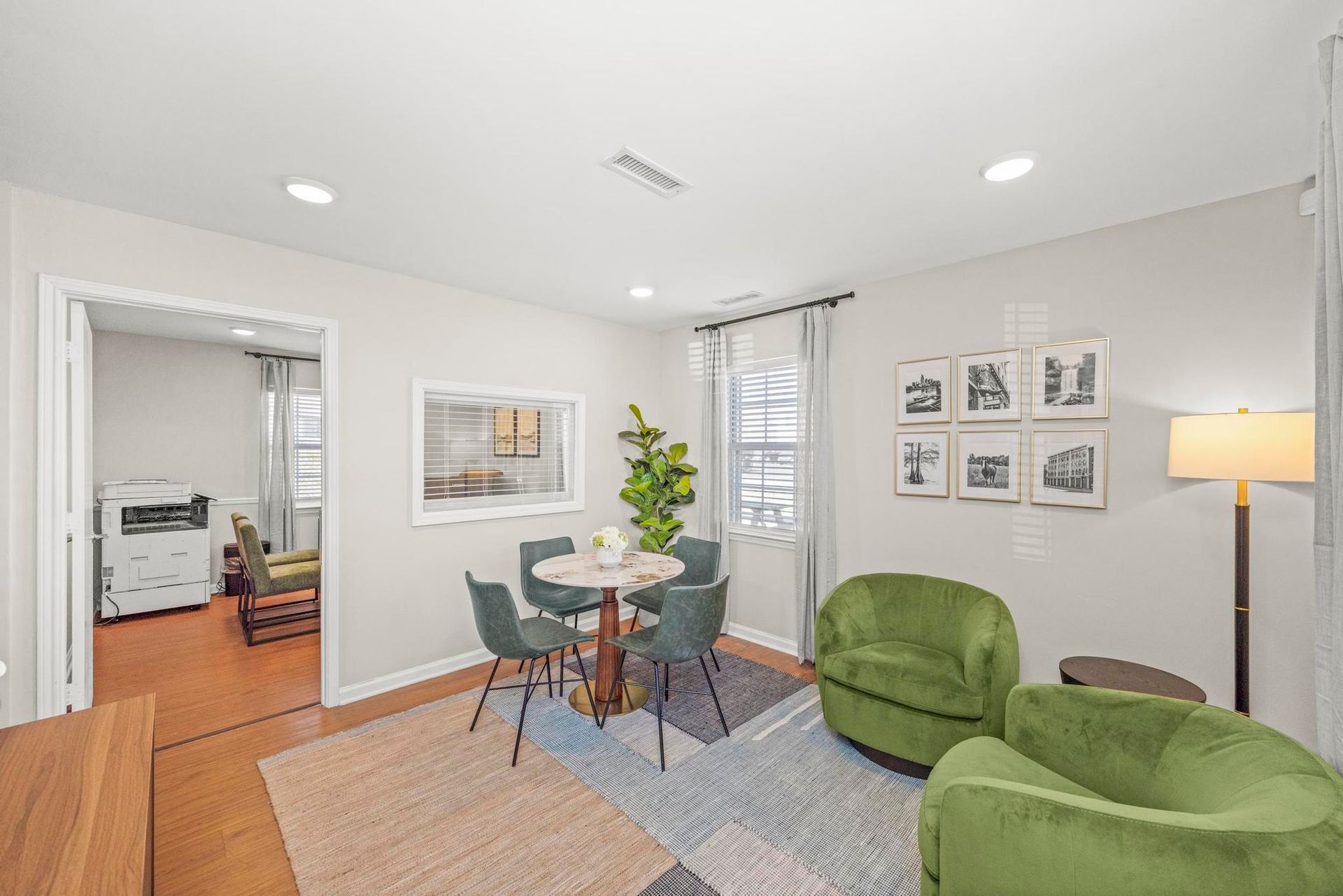 Bright living room with green chairs, glass table, floor lamp, and framed wall art near an open doorway