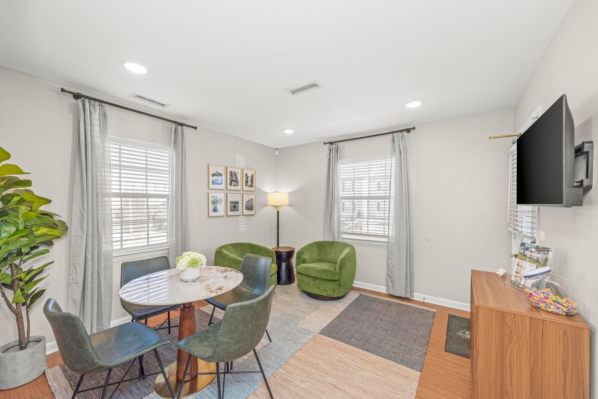 Bright living room with green chairs, small table, wall art, and a mounted TV near a window.