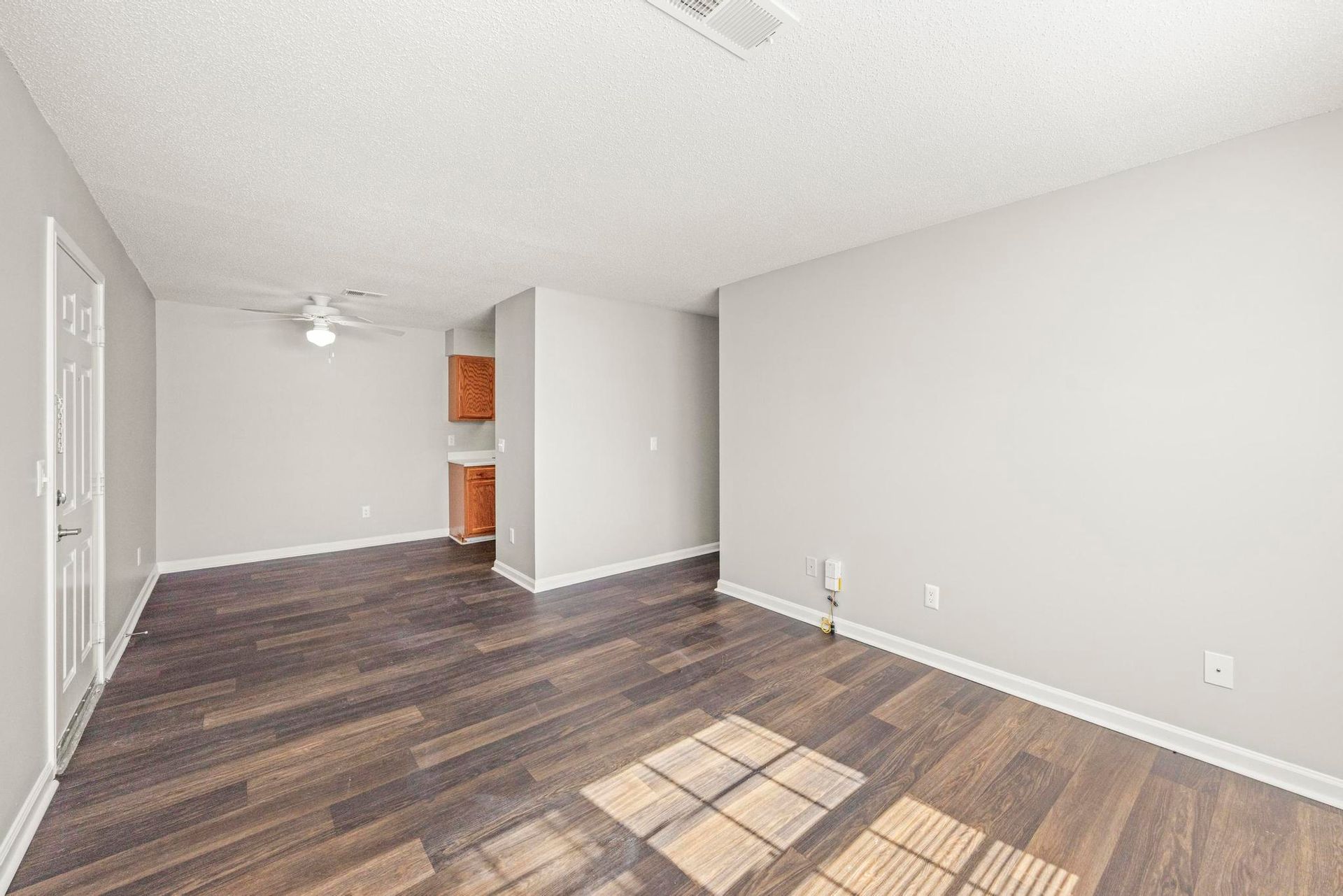 Empty white room with dark wood floors, recessed lighting, and a small alcove with shelving.