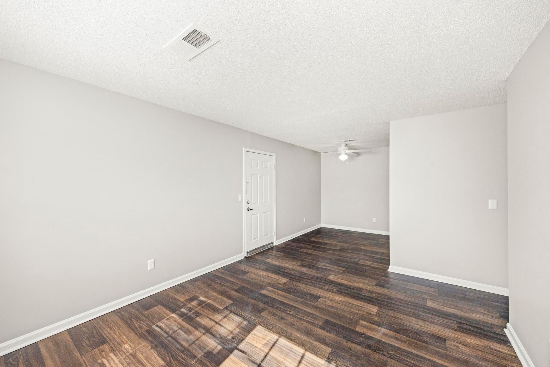 Empty room with light gray walls, white door, and dark wood-look flooring.