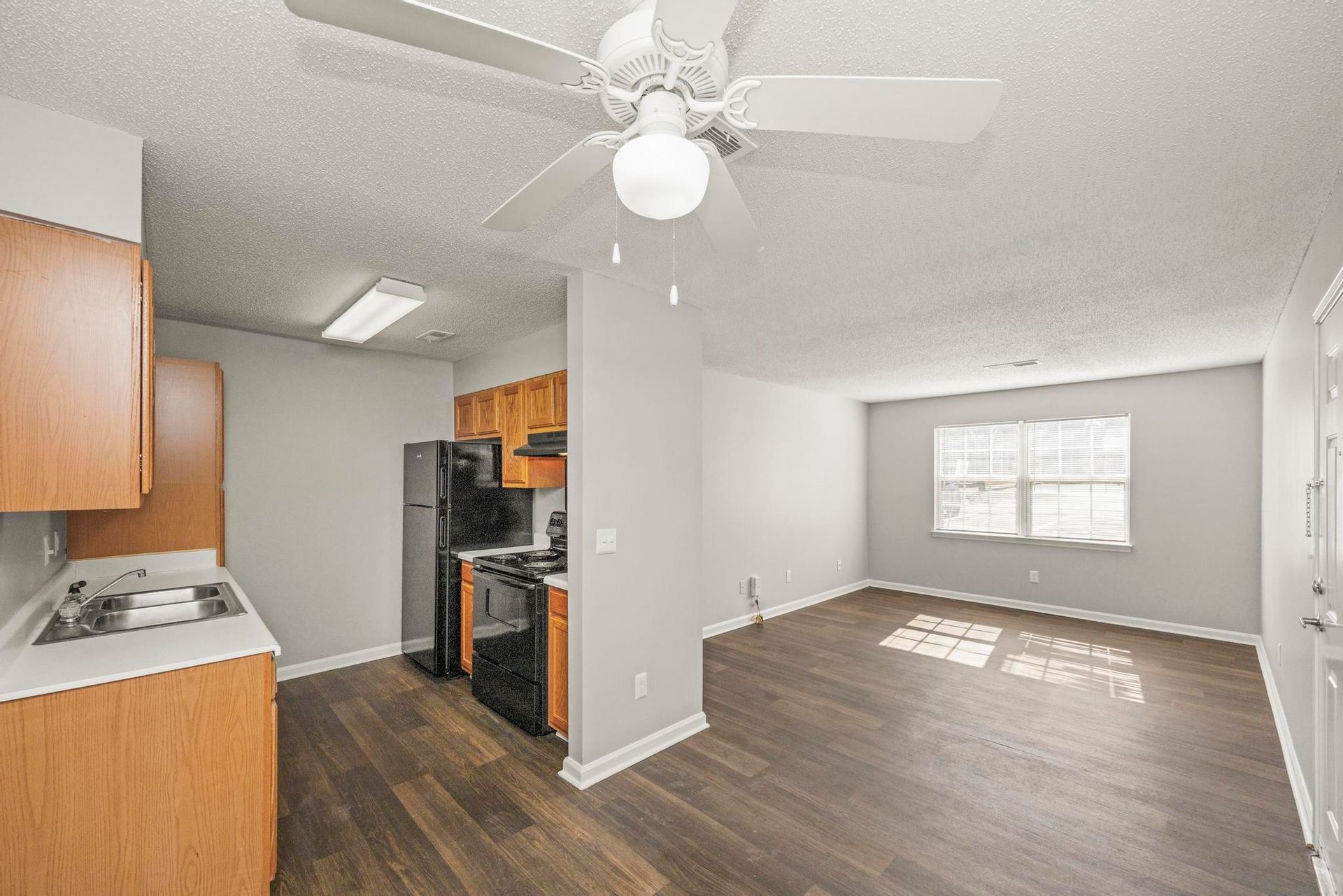 Open-plan kitchen and living room with dark wood floors, white walls, and a ceiling fan.