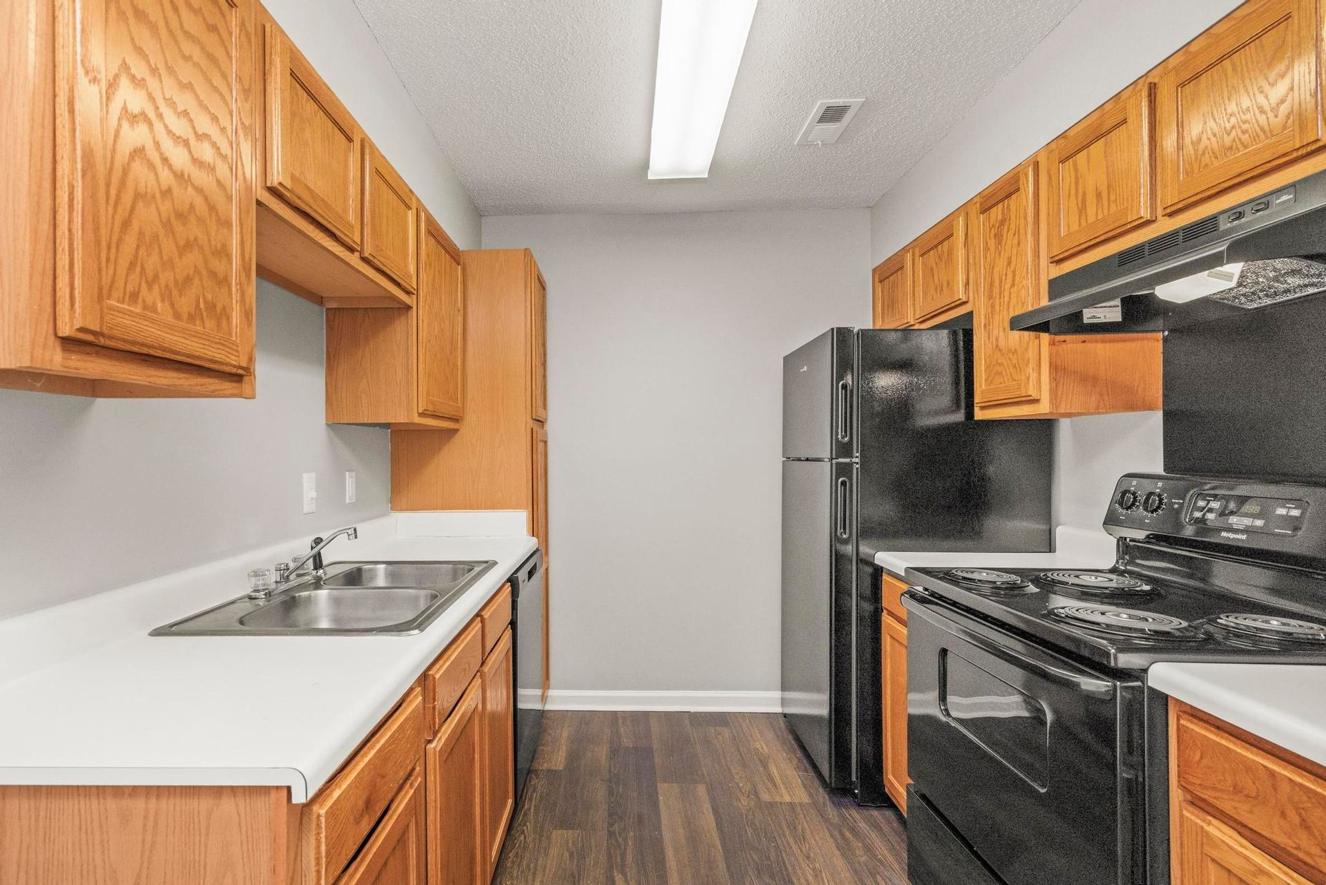 Narrow kitchen with wood cabinets, white countertops, black appliances, and wood-look flooring.