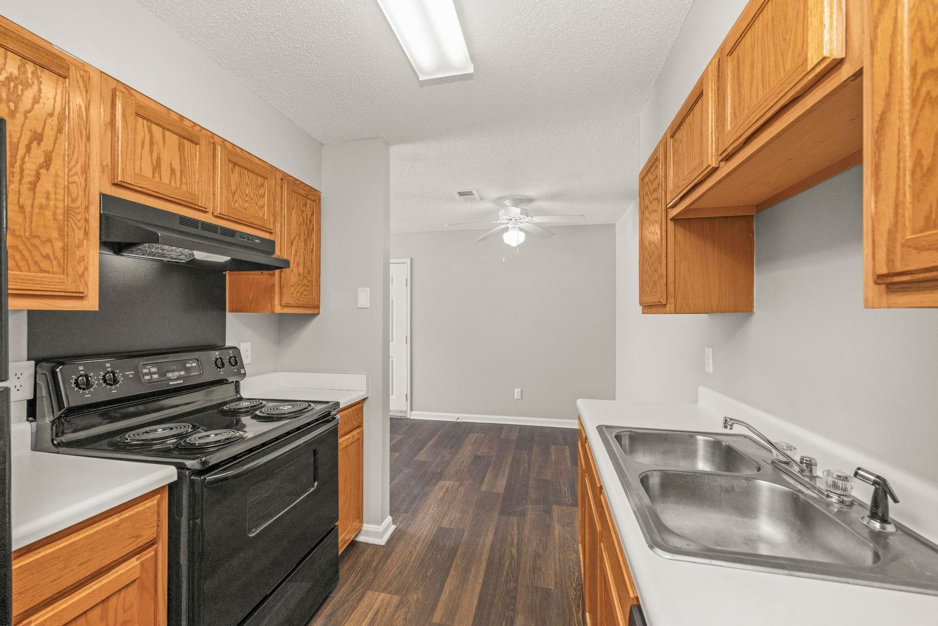 Small kitchen with wood cabinets, black stove, white countertops, and stainless steel sink.