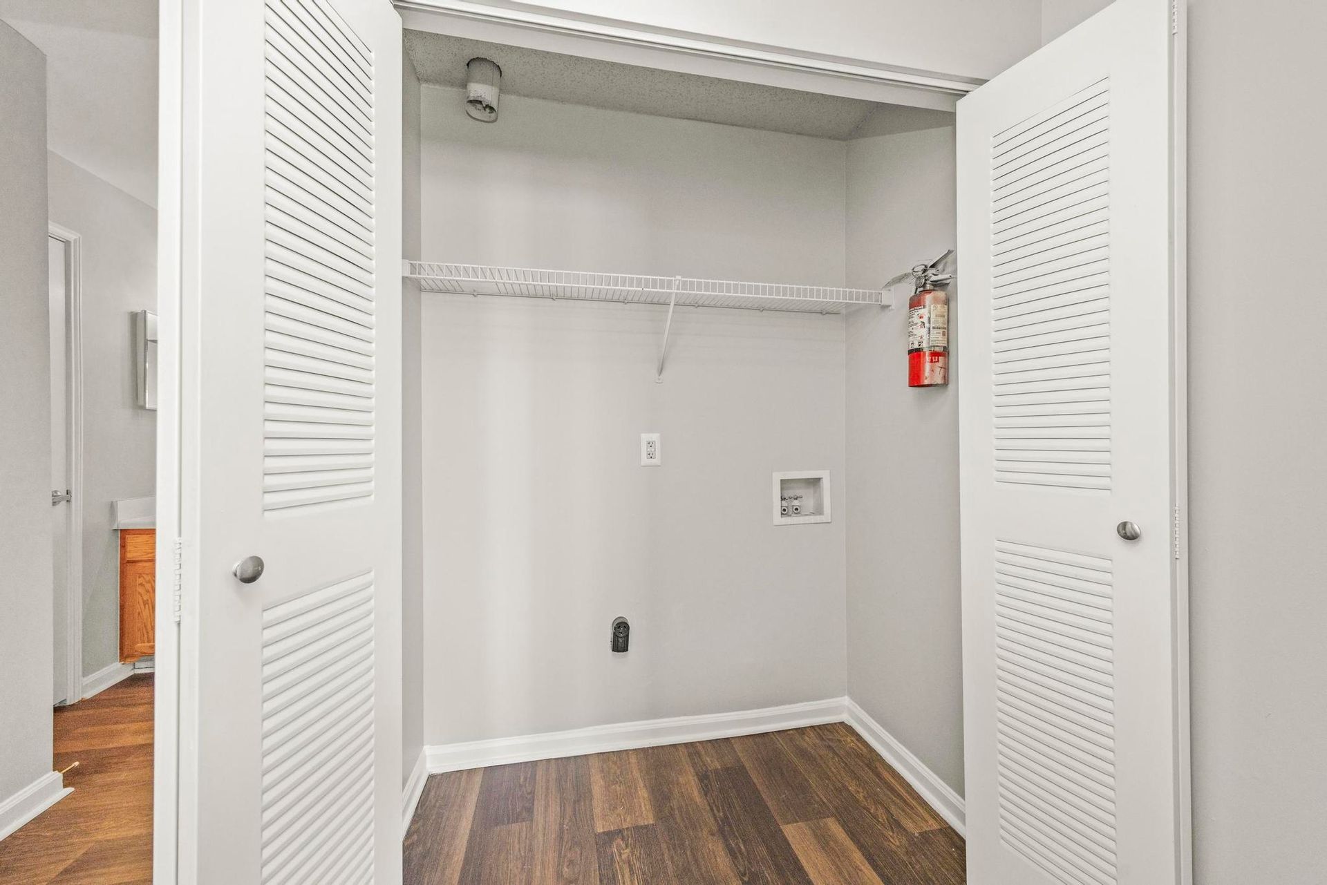 Open closet with white louvered doors, wire shelf, gray walls, and wood floor.