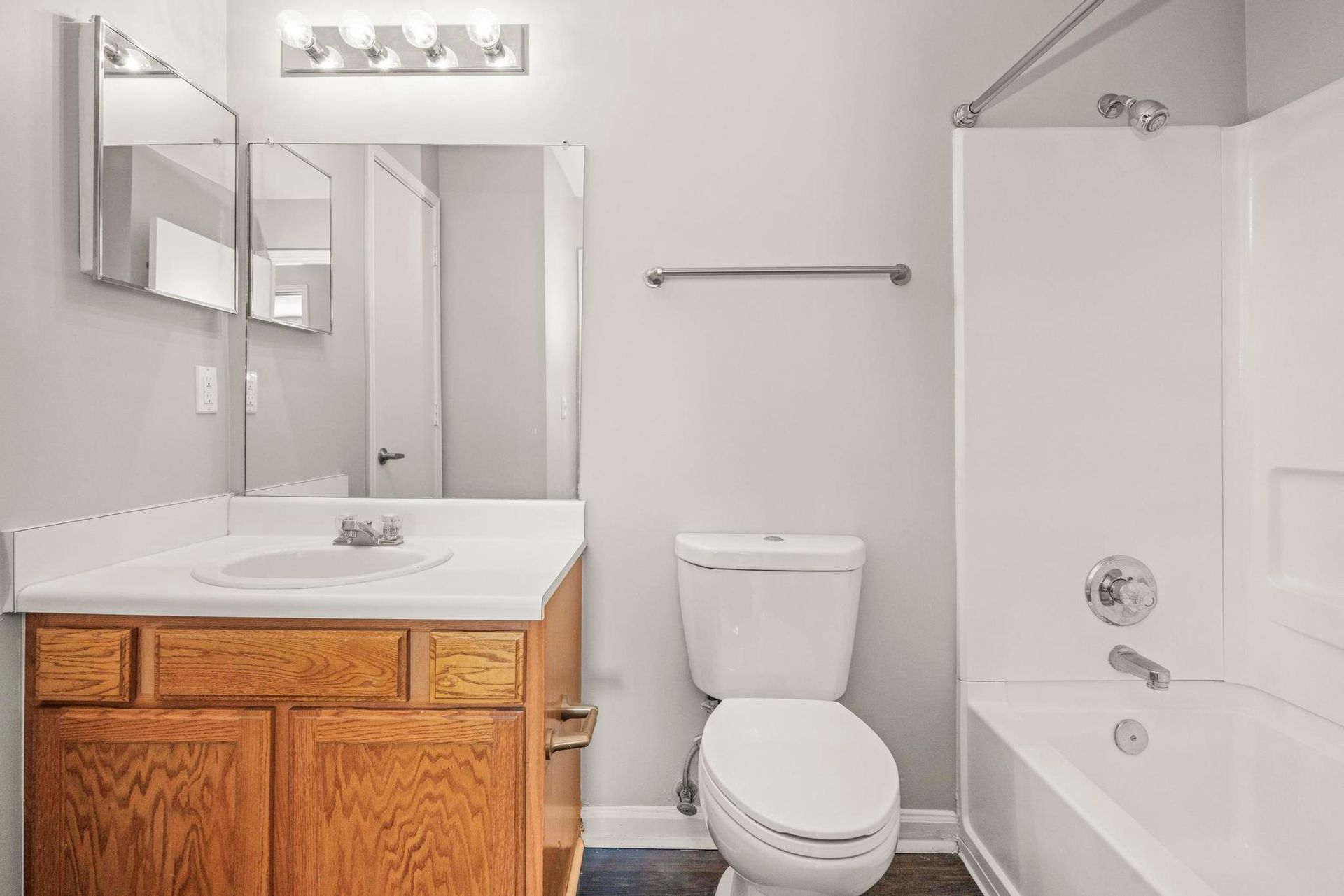 Small bathroom with wooden vanity, toilet, mirror, and white shower/tub.