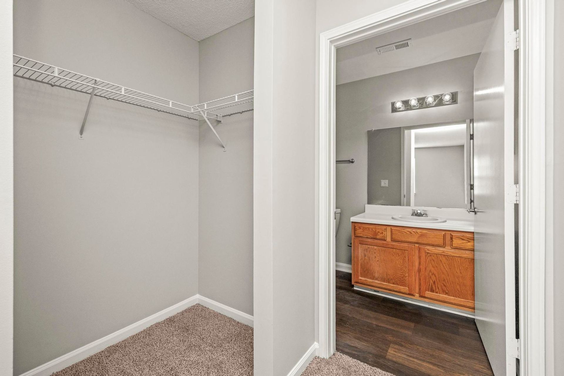 Empty walk-in closet beside a bathroom with white walls, wire shelving, and beige carpet.