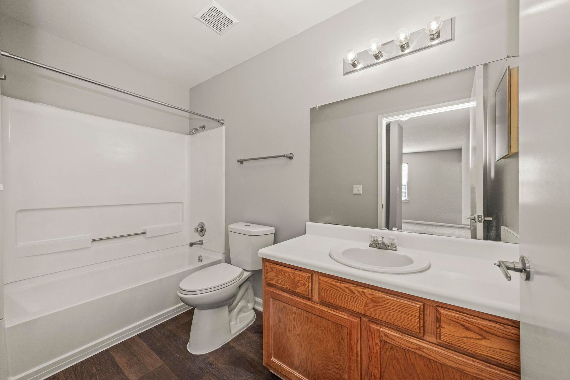 Bright bathroom with white tub, toilet, and wooden vanity with mirror.