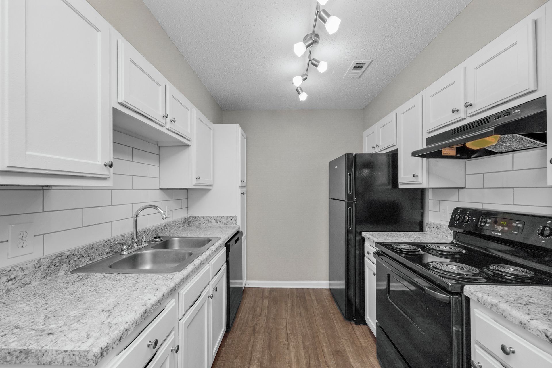 Bright white galley kitchen with black appliances, granite counters, and wood-look flooring